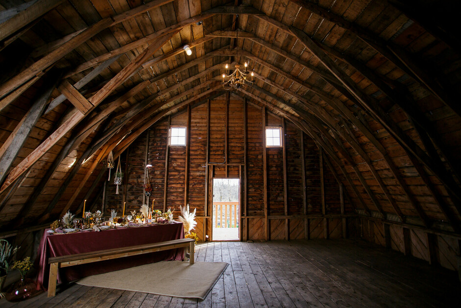 An old rustic barn that is decorated with event rentals, tables, place setting, linen and flowers.