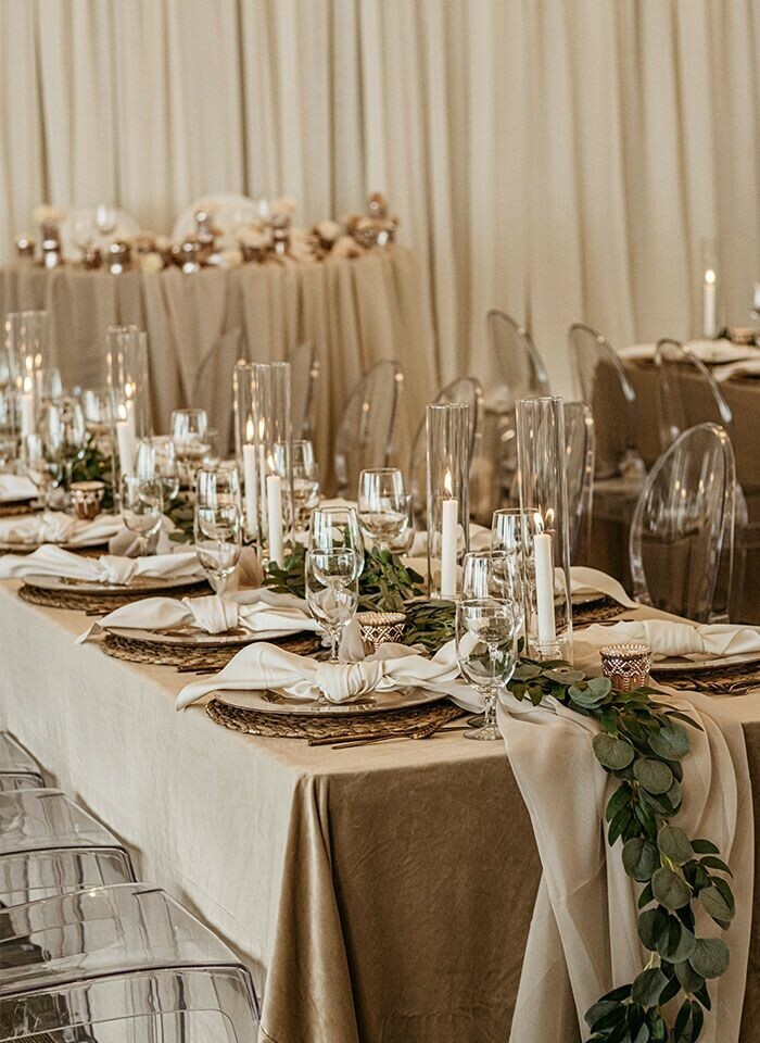 Special Event Rentals - Edmonton event table covered in cashmere velvet tablecloth, green garland and cheesecloth runner, lit candlesticks in tall cylinder glass vase, and gold ivory tableware