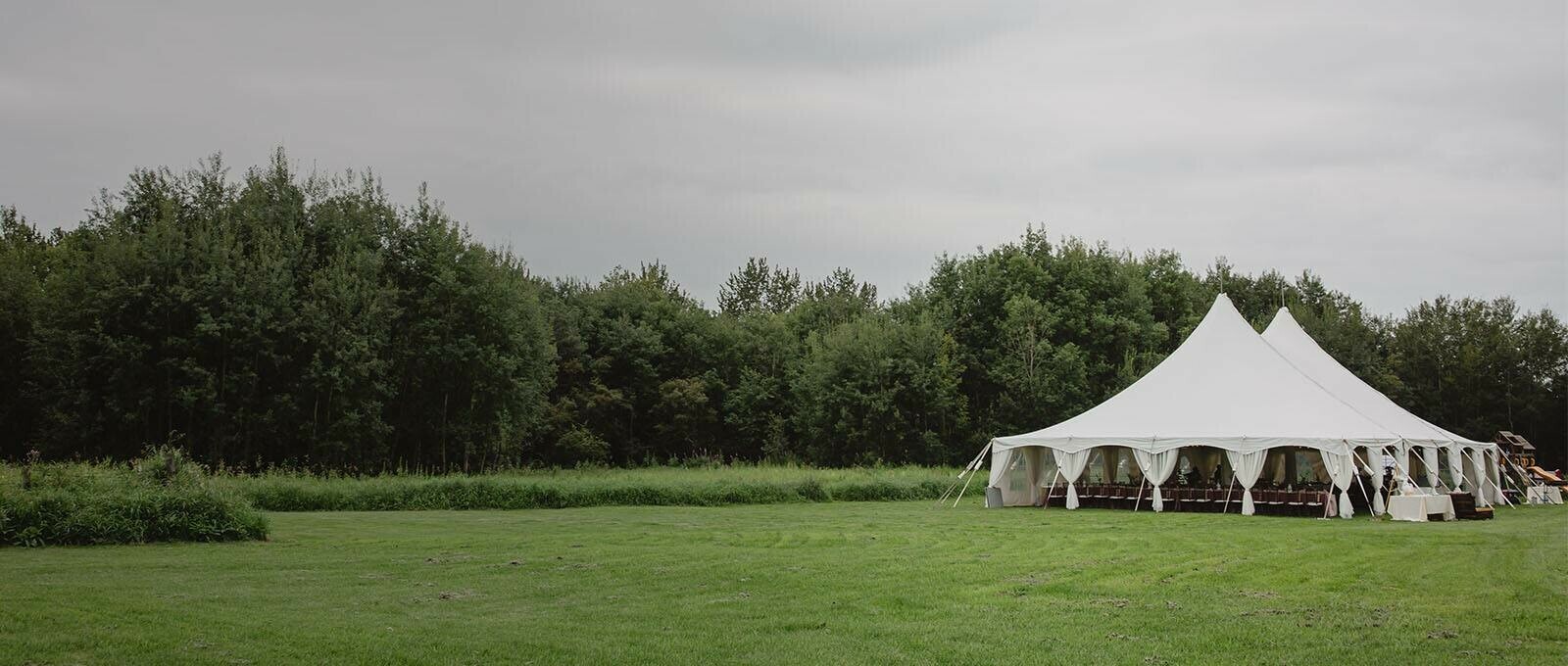 Tent Rentals Edmonton showcasing a white pole circus tent on a wide greenland with a green trees on the background