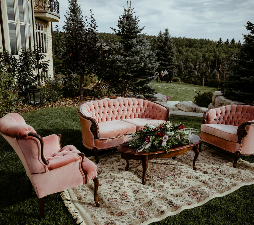 Pink Sofa Chairs and a Pink Sofa with a brown table set up with a brown pattern rug underneath set up for a outdoor wedding